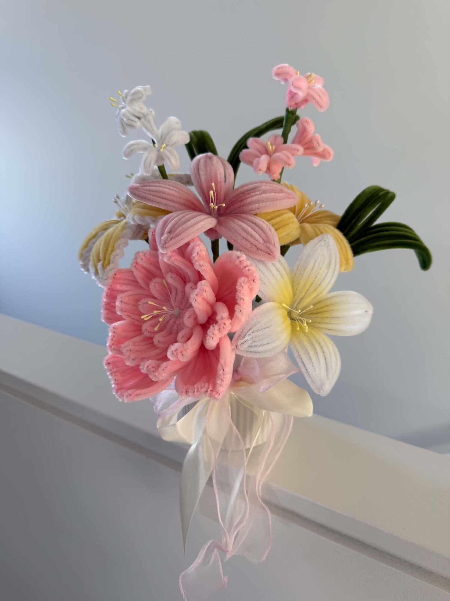 A handmade pipe cleaner bouquet of pink, cream and yellow flowers tied with a ribbon